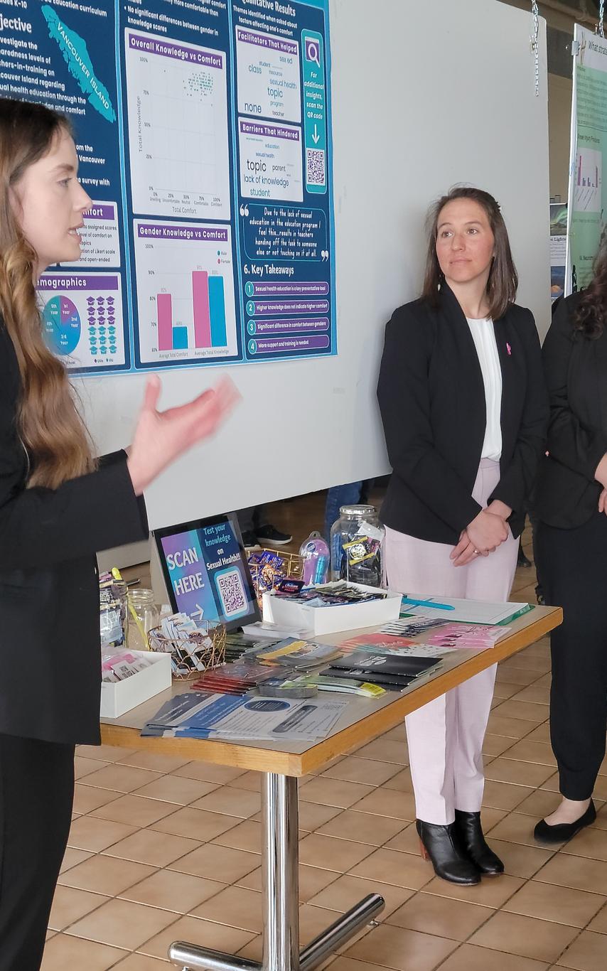 Four professionally dressed female students in front of a research poster facing a faculty member