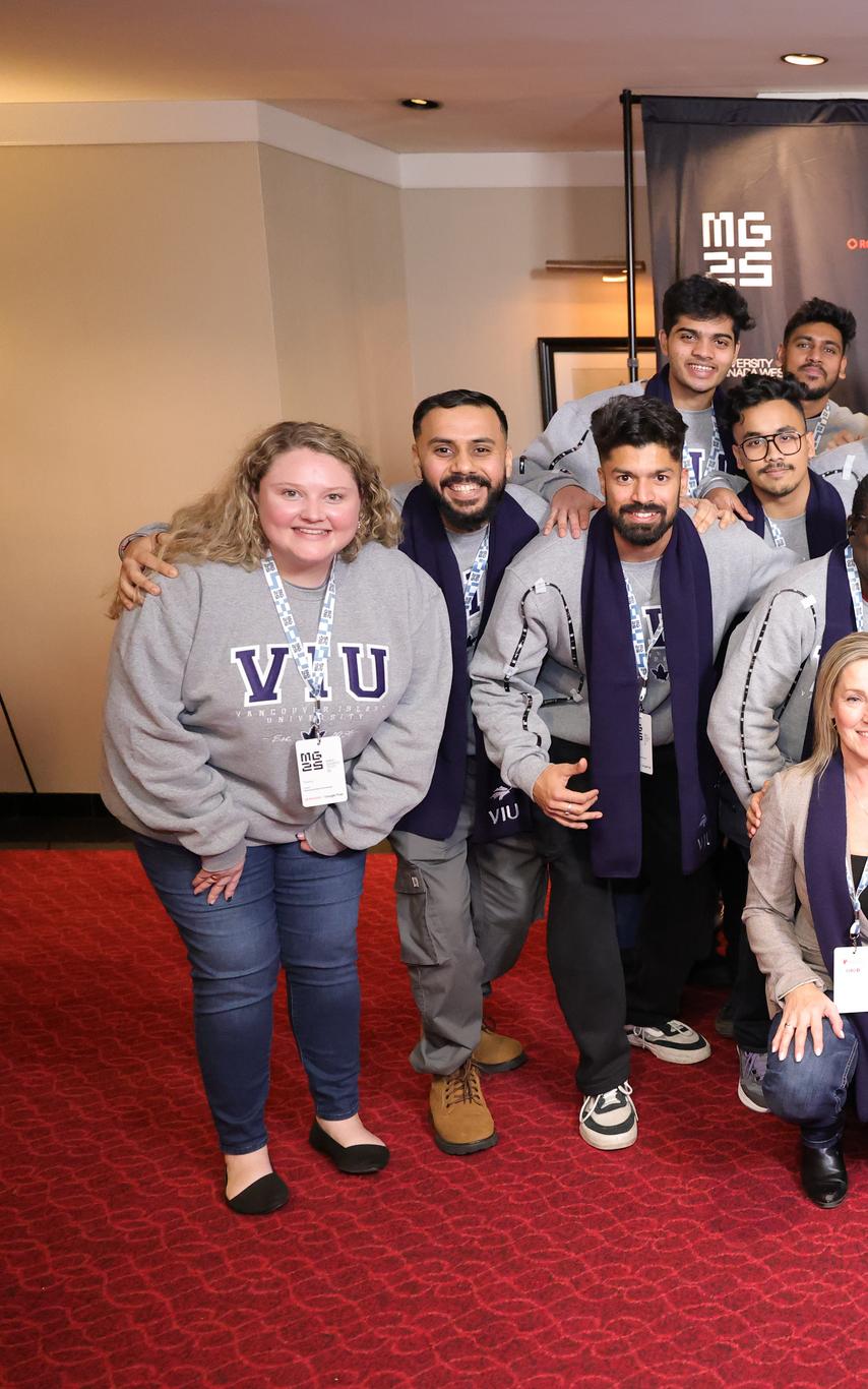 A group of 20 multicultural and multinational MBA students with three faculty coaches crouching in three rows with a the MBA games 25 sign background